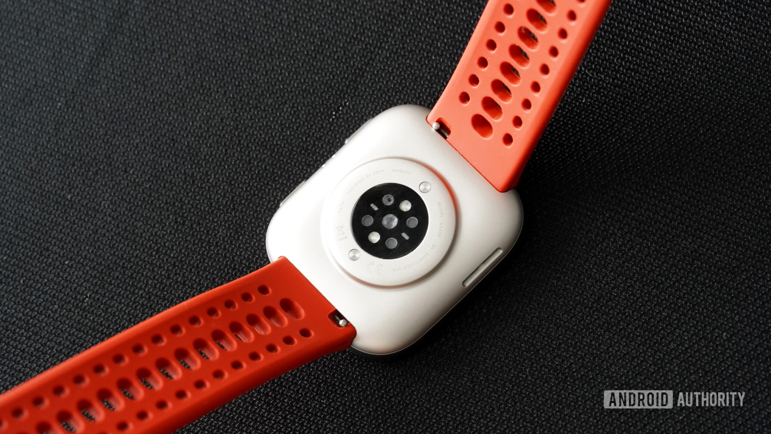 An Amazfit Bip 6 rests facedown displaying its sensors and quick-release band mechanisms.