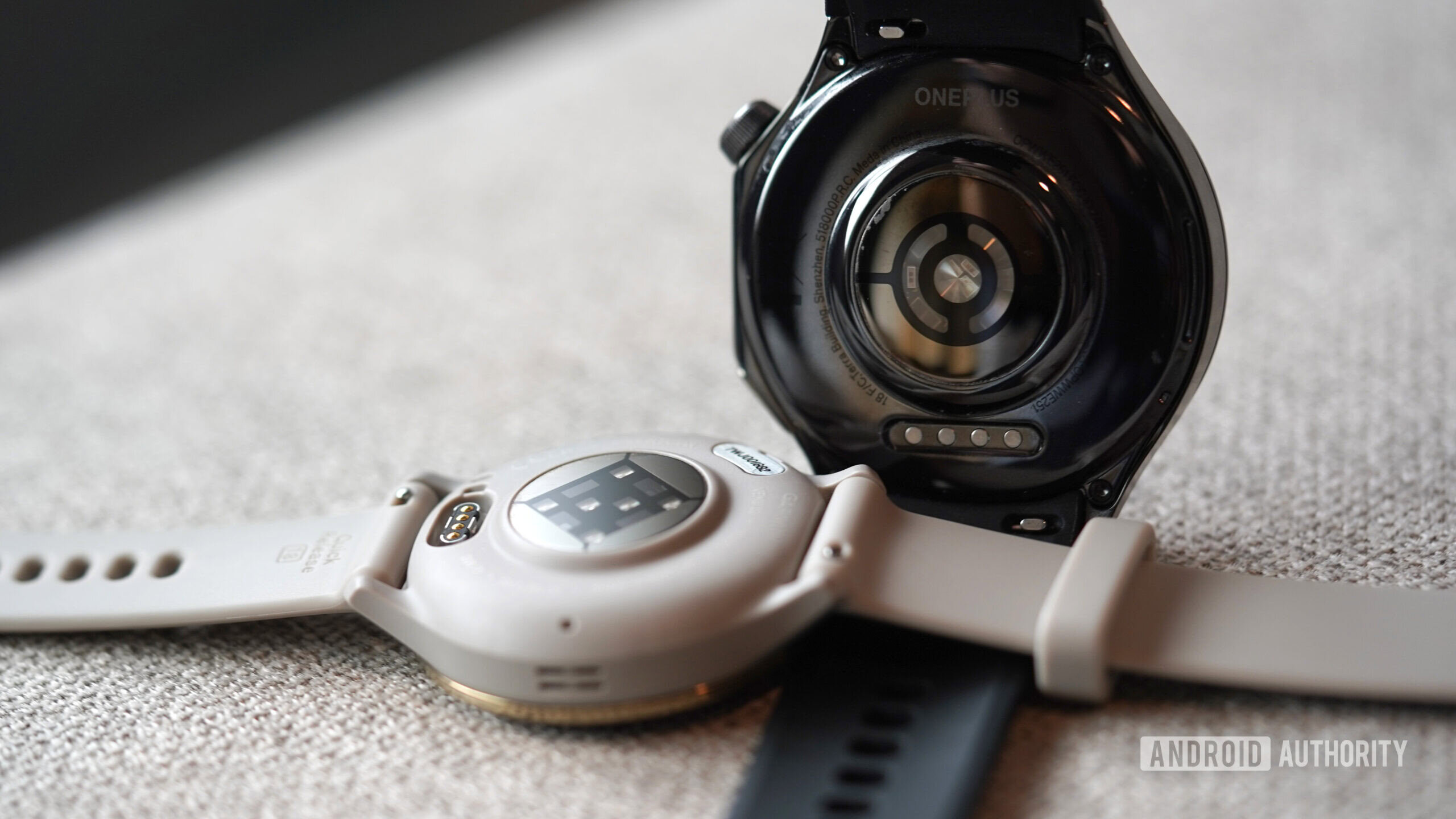 Garmin Venu 3 vs OnePlus Watch 3 A Garmin Venu 3 and OnePlus Watch 3 rest face down displaying their sensor packages.
